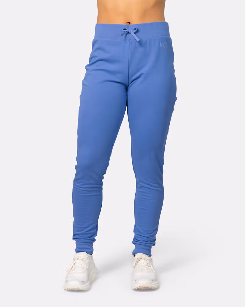 Woman modeling the Kari Traa Kari Pant in sea blue, showing its slim-fit style and ribbed cuffs for lounging.