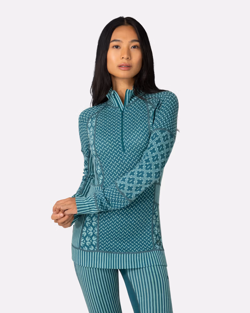 Woman wearing the teal Kari Traa Smekker Half Zip Base Layer, showing the jacquard-knit panels and zip neck.