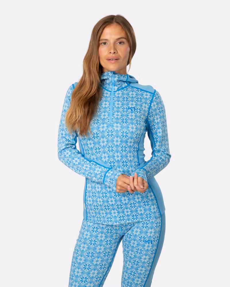 Woman wearing the light blue Kari Traa Rose Base Layer Hoodie with a Nordic pattern, showing the slim fit and lined hood.