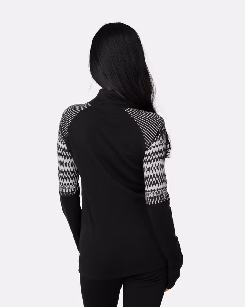 Back view of a woman in the black Kari Traa Silja 2.0 Half Zip, showing the solid black back and patterned arms.