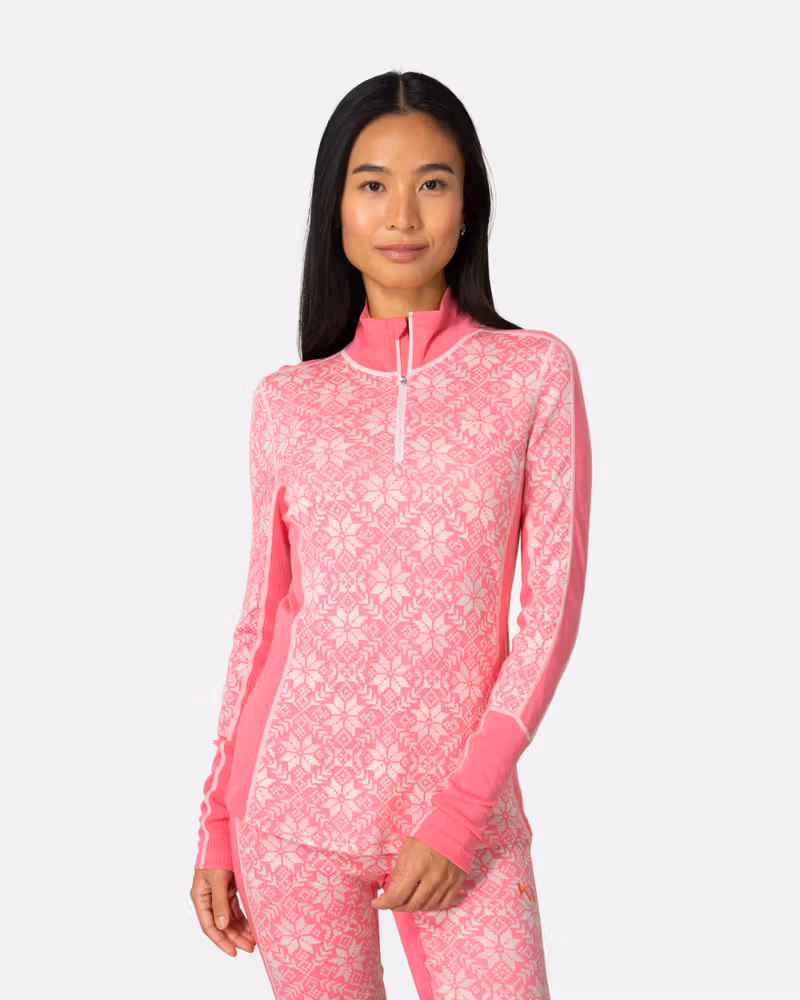 Front view of woman in Kari Traa Anna Half Zip in pink with Nordic snowflake print, merino wool base layer