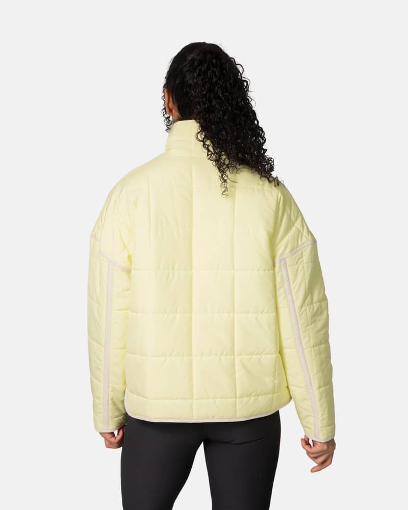 Back view of a woman in the light yellow Kari Traa Mina Jacket, showing the loose fit and quilted padding for warmth.