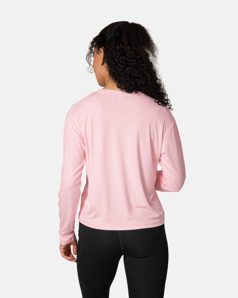 Back view of a woman in the pastel pink Kari Traa Una Long Sleeve, showing its relaxed fit for sun-drenched adventures.