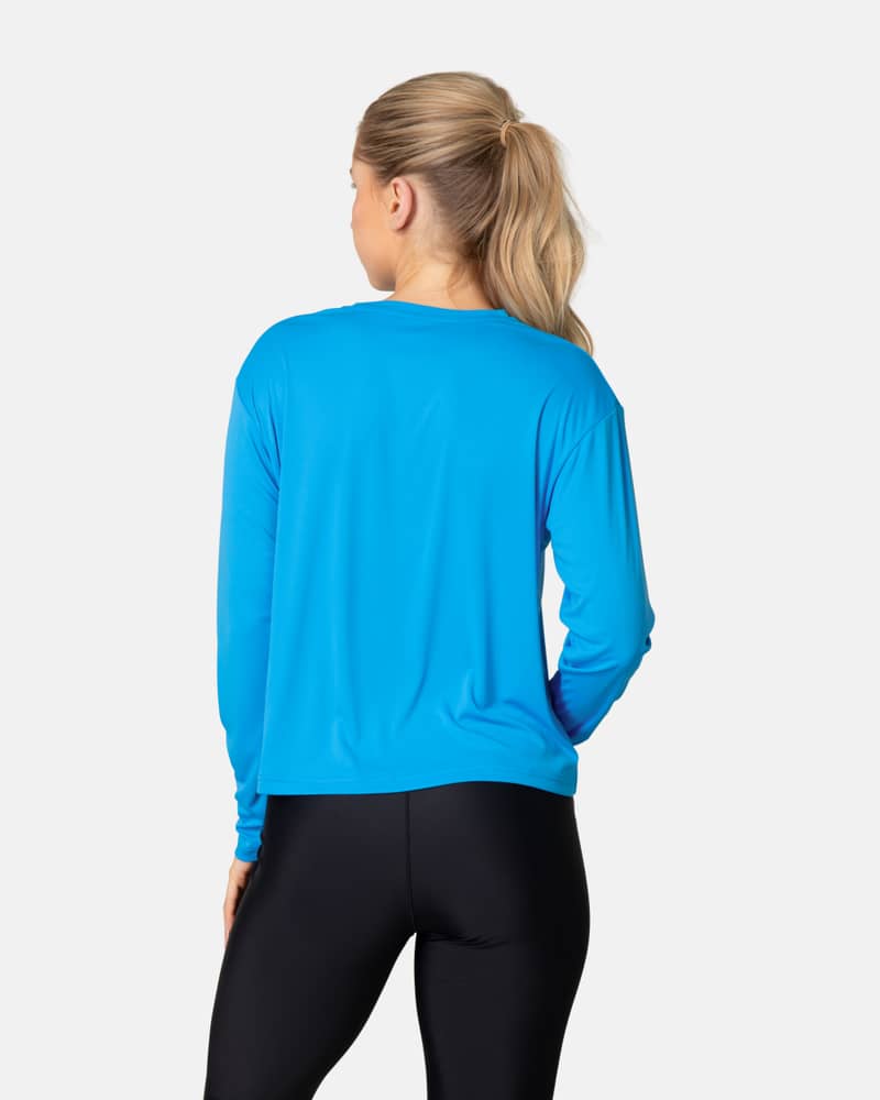 Back view of a woman in the blue horizon Kari Traa Una Long Sleeve, showing the relaxed fit for outdoor adventures.
