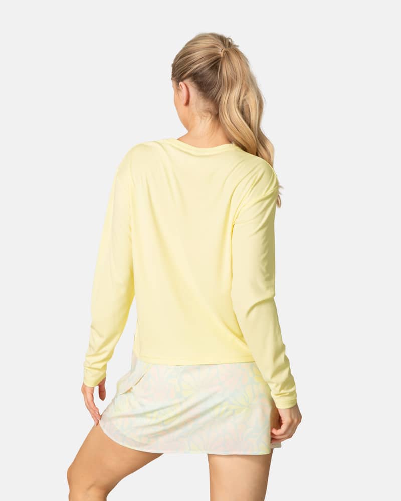 Back view of a woman in the light yellow Kari Traa Una Long Sleeve, showing its relaxed fit for sun-drenched adventures.