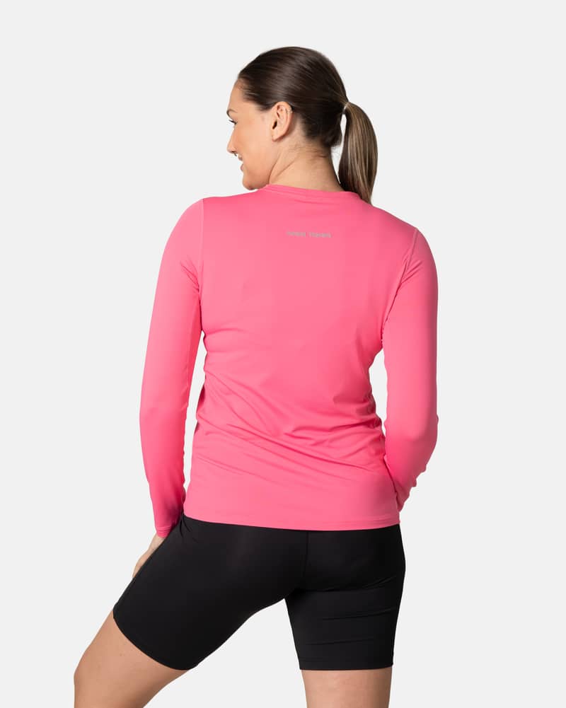 Back view of a woman in the bright pink Kari Traa Ava Long Sleeve, showing the reflective logo detail for visibility.