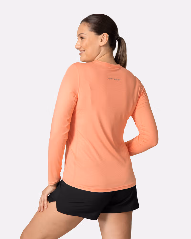 Back view of a woman wearing the peach blossom Kari Traa Ava Long Sleeve, showing the reflective logo for visibility.