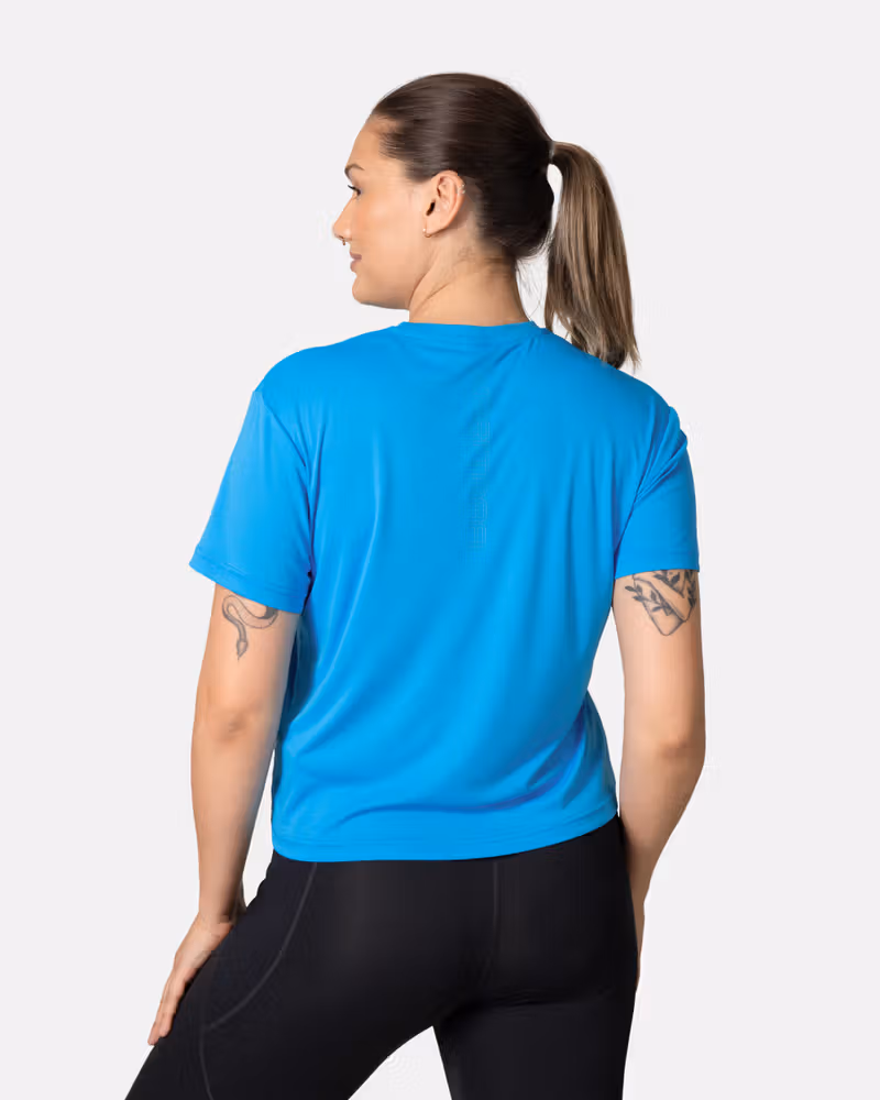 Back view of a woman in the blue Kari Traa Una Tee, highlighting the vertical logo and relaxed fit for active comfort.