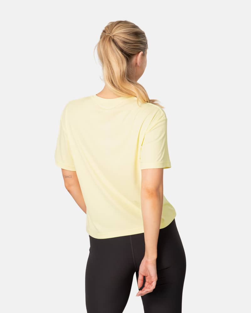 Back view of a woman in the yellow Kari Traa Una Tee, showing its relaxed fit for active comfort.