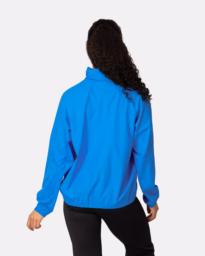 Back view of a woman in the bright blue Kari Traa Nia Wind Jacket, showing its comfortable, loose fit for easy movement.