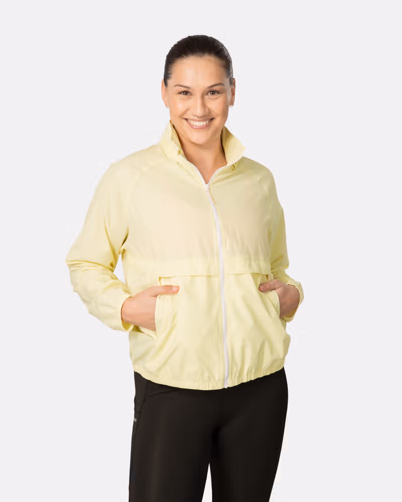 Woman wearing the light yellow Kari Traa Nia Wind Jacket, showcasing its loose fit and front pockets for outdoor activities.