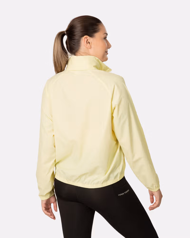 Back view of a woman in the light yellow Kari Traa Nia Wind Jacket, highlighting its protective high collar and fit.