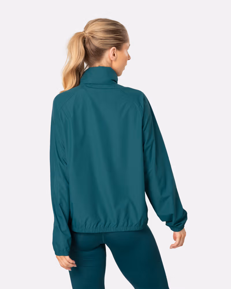 Back view of a woman in the peacock Kari Traa Nia Wind Jacket, showing the raglan sleeves and loose fit.